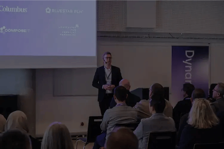 Speaker presenting at a DynamicWeb event to an audience, with Truvio partner logos displayed on the presentation screen.