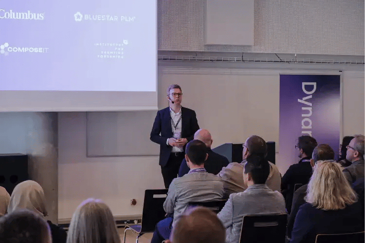 Speaker presenting at a DynamicWeb event to an audience, with Truvio partner logos displayed on the presentation screen.