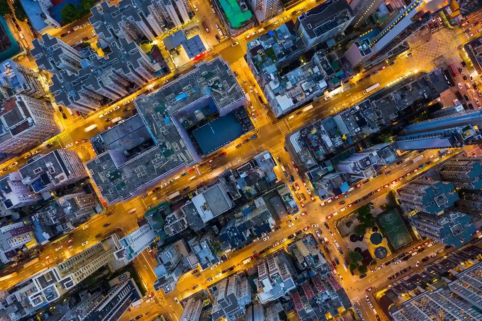 Aerial top-down view of a busy city intersection at night with illuminated streets, high-rise buildings, and traffic.