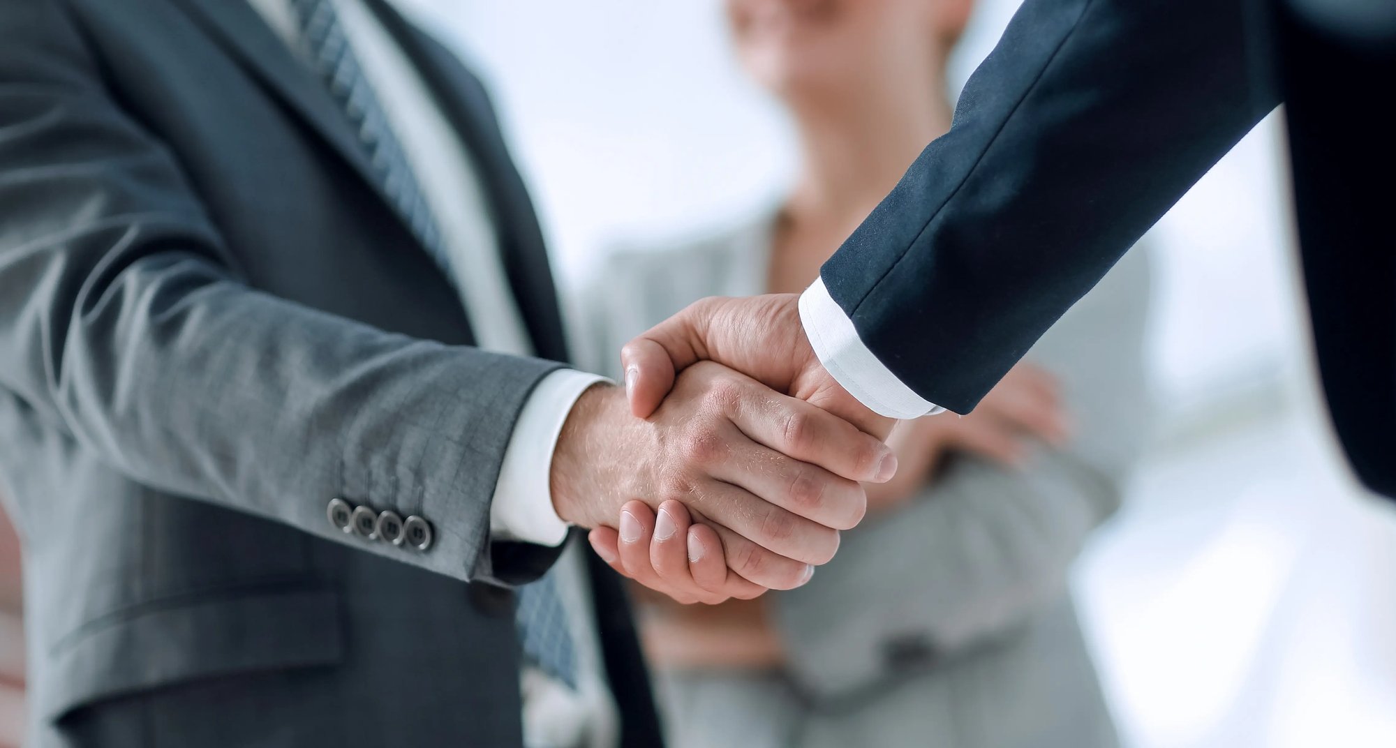 Close-up of two business professionals shaking hands, symbolizing a successful agreement, with colleagues blurred in the background.
