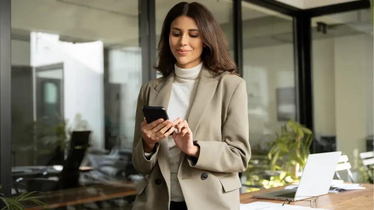 Businesswoman checking her smartphone while standing in a modern office workspace.