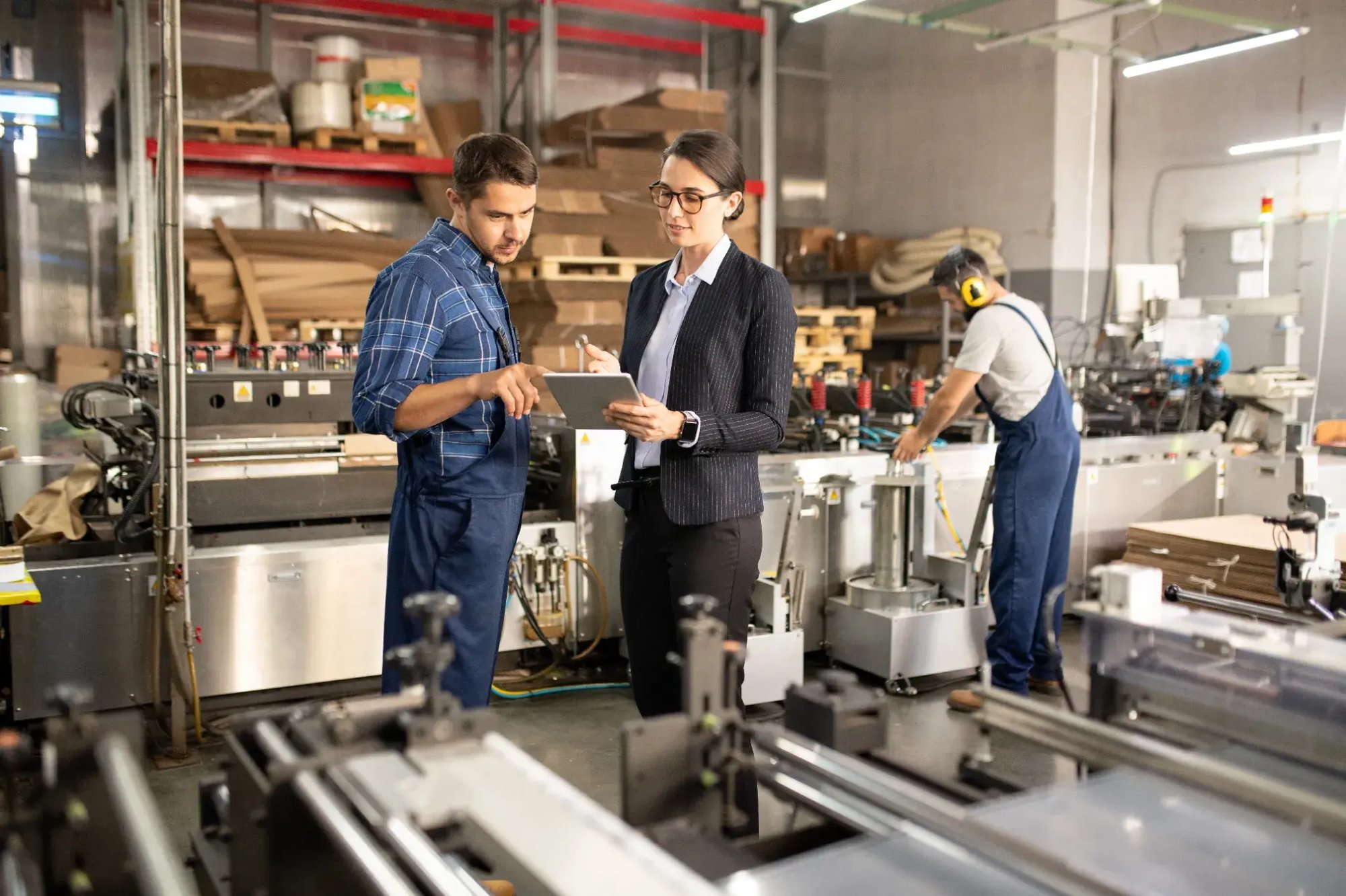 A factory supervisor and a production worker reviewing information on a tablet on a manufacturing floor.