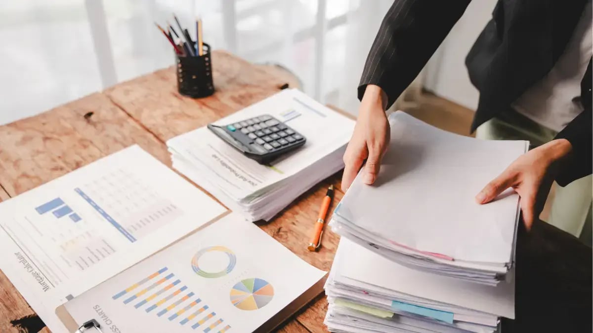 Professional organizing financial documents and reports with charts and calculator on a desk.