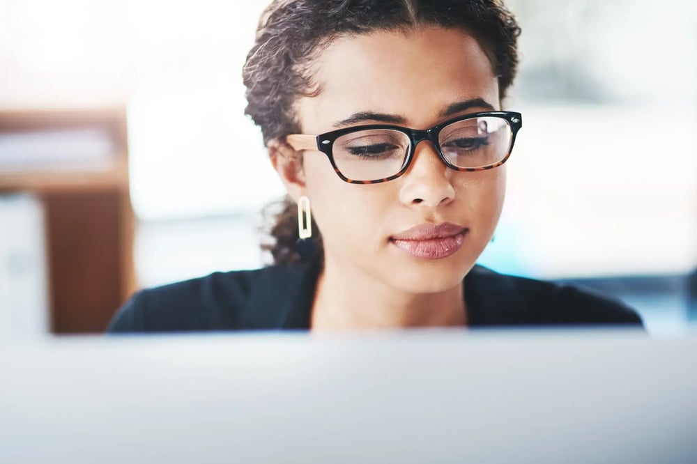 Close-up of a professional wearing glasses working on a laptop in a bright modern office setting.